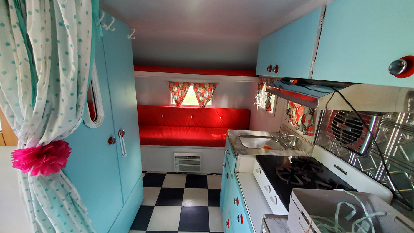 Cozy, retro camper interior with a red dinette, kitchenette, and checkered floor, ideal for your next RV rental.