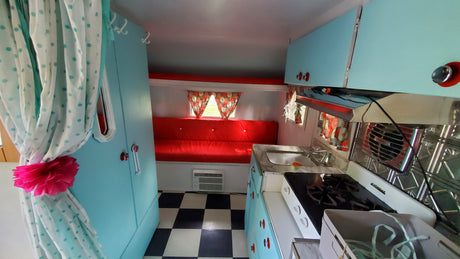 Cozy, retro camper interior with a red dinette, kitchenette, and checkered floor, ideal for your next RV rental.