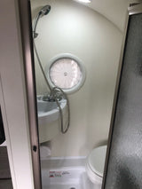 RV rental wet bath: compact shower, sink, and toilet with a unique round window.