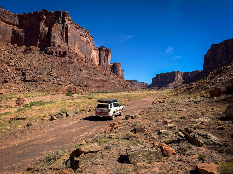  showing the steering wheel and dashboard with a scenic road ahead. Perfect for an RV rental trip.|White TRD Off Road SUV with rooftop tent on dirt road — photo 8
