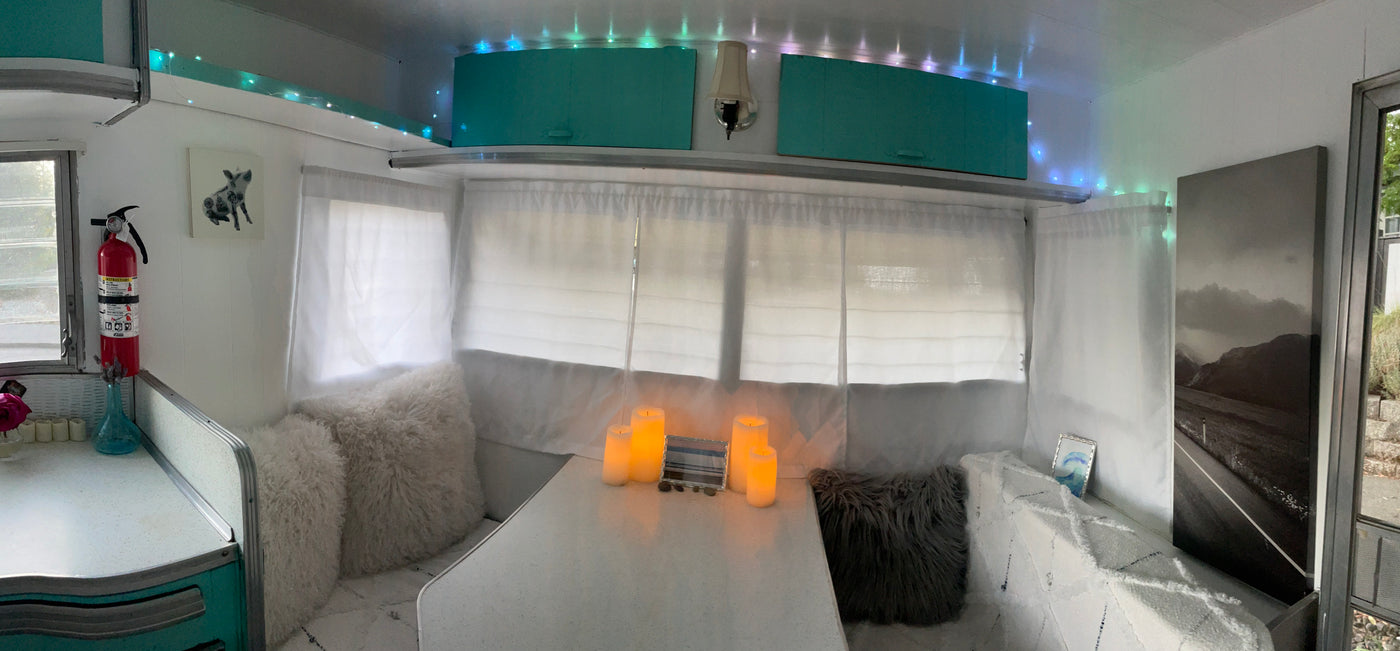 Inside a cozy RV rental: white dining booth, faux candles, teal cabinets, and soft lighting for a comfortable travel experience. — photo 15