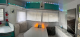 Inside a cozy RV rental: white dining booth, faux candles, teal cabinets, and soft lighting for a comfortable travel experience.