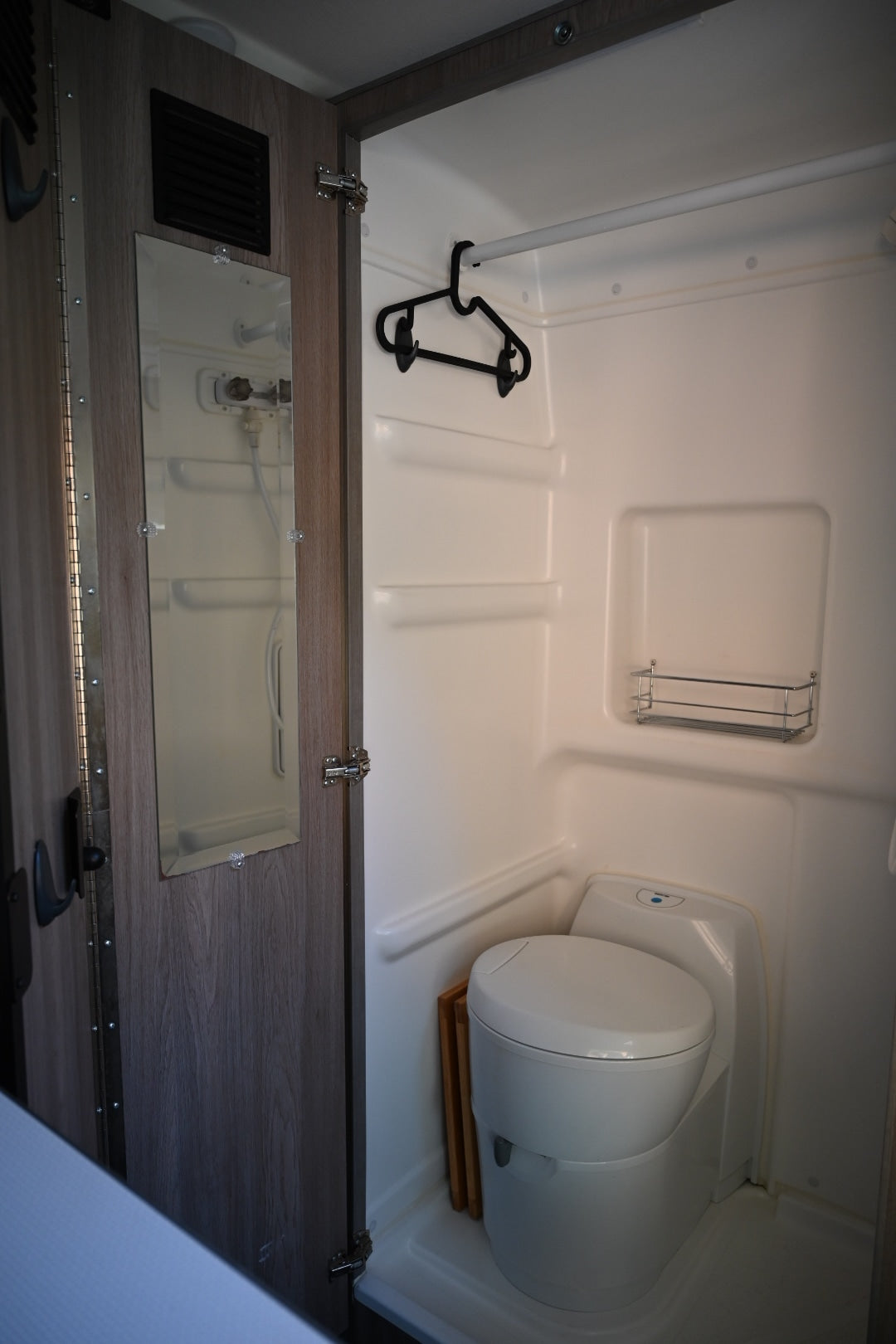 Compact RV rental wet bath featuring a toilet, shower, hanging rod, and mirror on the door.