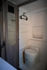 Compact RV rental wet bath featuring a toilet, shower, hanging rod, and mirror on the door.