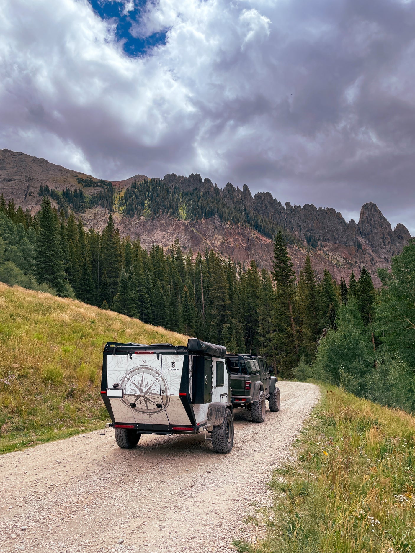 Off-road rv rental: A rugged trailer towed by a truck on a scenic mountain road under cloudy skies.