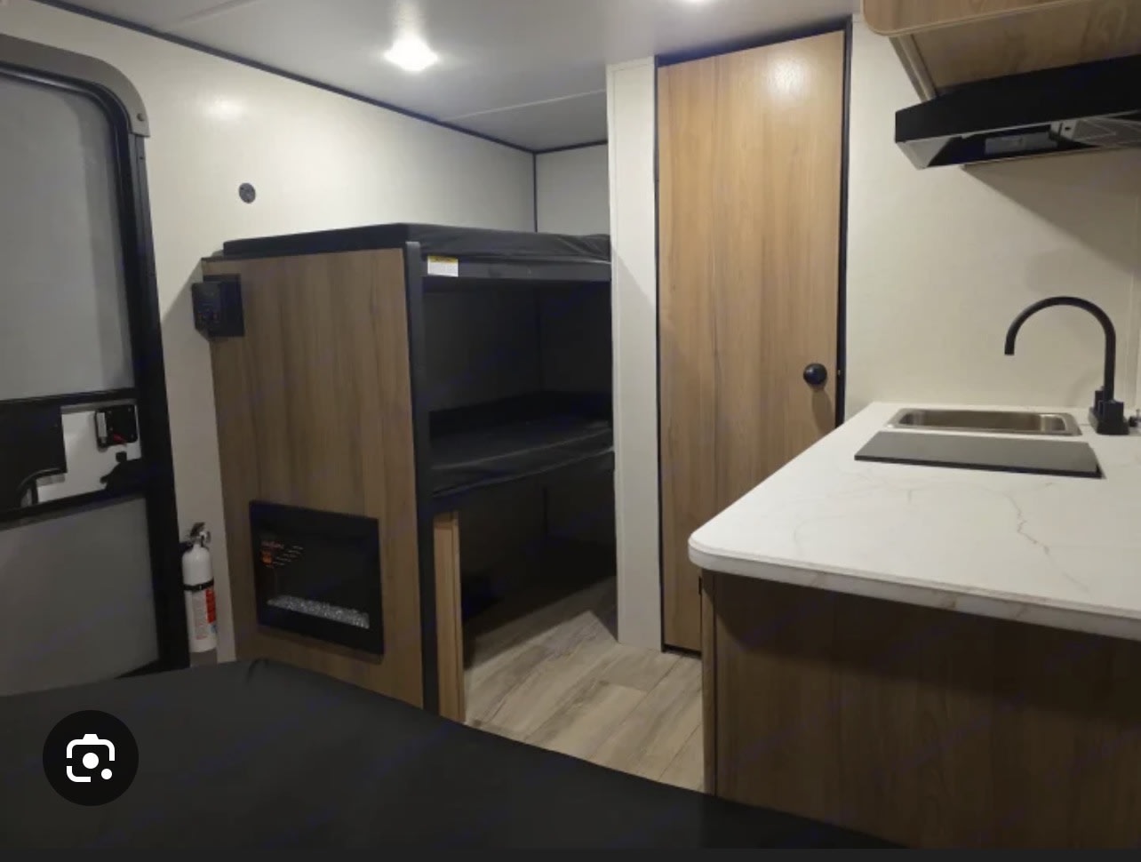 Inside an RV rental: a cozy kitchen counter with sink, bunk beds with a small fireplace, and a light-wood door.