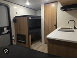Inside an RV rental: a cozy kitchen counter with sink, bunk beds with a small fireplace, and a light-wood door.