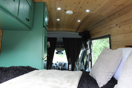Cozy rv rental camper van interior with a bed, green cabinets, wooden ceiling, and wine set up for a relaxing trip.