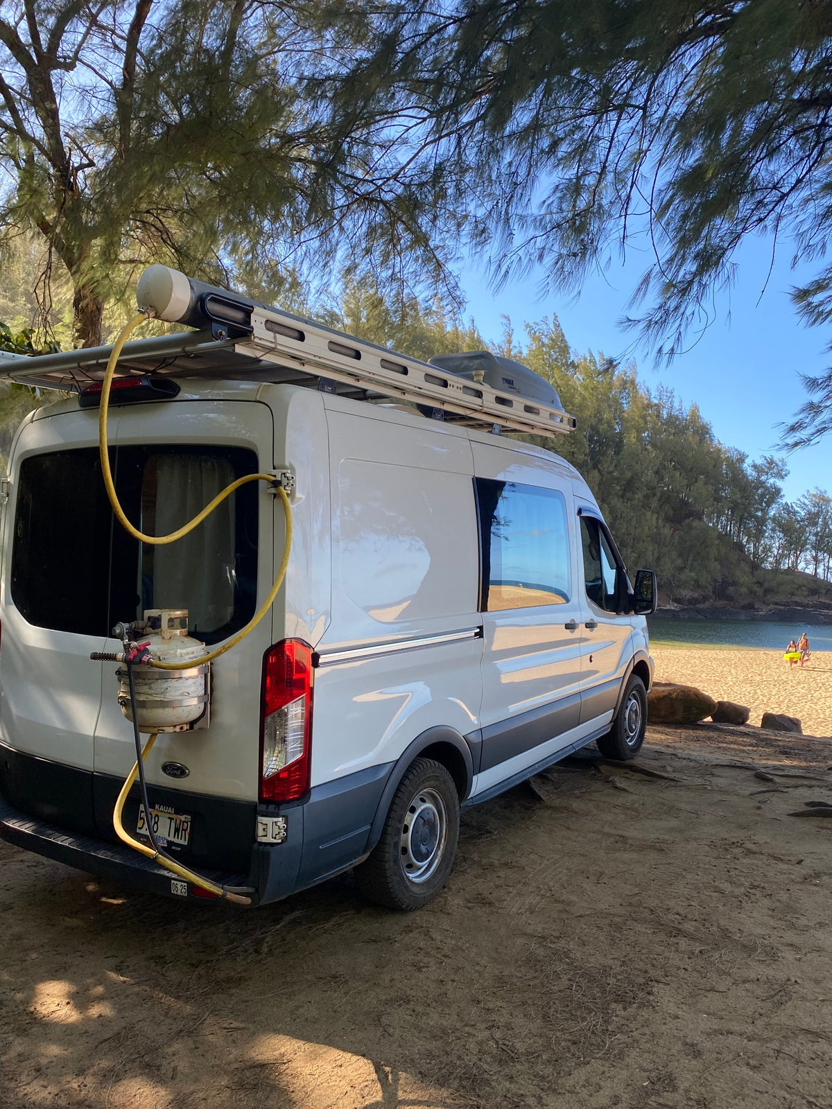 White Ford Transit rv rental camper van parked on a beach, equipped with a roof rack and outdoor shower. — photo 2