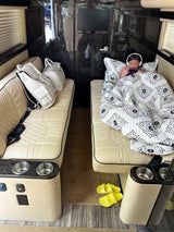 Relax in an **RV rental**! A child is cozy under a blanket on a plush bench with headphones, beside luxury bags.