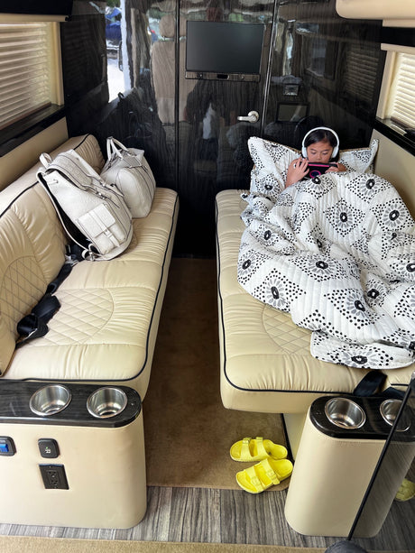 Relax in an **RV rental**! A child is cozy under a blanket on a plush bench with headphones, beside luxury bags.