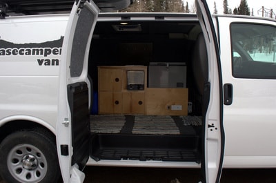 Open doors of an rv rental camper van reveal a practical custom interior with wood storage, fridge, and heater. — photo 6