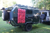 Off-road RV rental: Dark green overland trailer with recovery gear hitched to an Ineos Grenadier, ready for adventure.