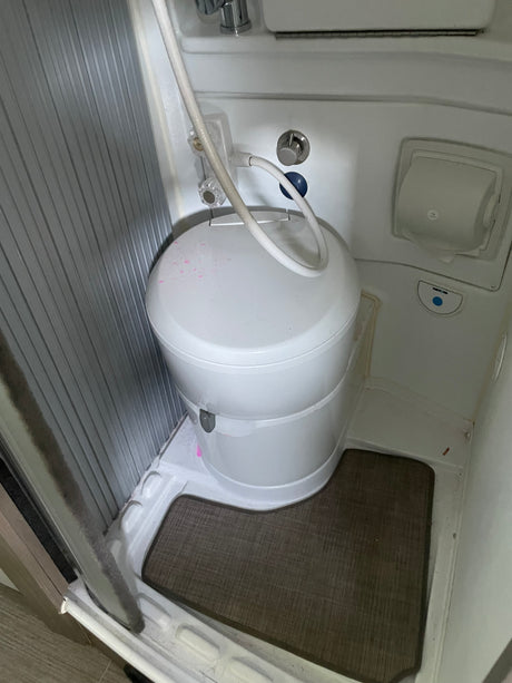 RV rental: Compact bathroom with white toilet, shower hose, and wall-mounted accessories in a small space.