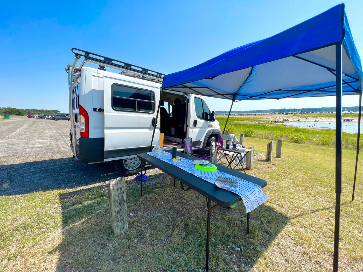 RV rental enjoying a sunny day. White van, blue canopy, tables set up by a lake with people enjoying the water. — photo 20