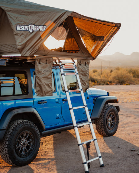 Blue Jeep with a Desert Armor rooftop tent & ladder, perfect for an RV rental or overlanding adventure.