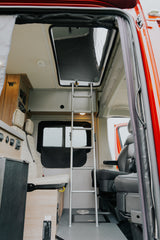 Inside an RV rental: a ladder to a pop-top bed, plush seating, and wooden cabinetry with control panels.
