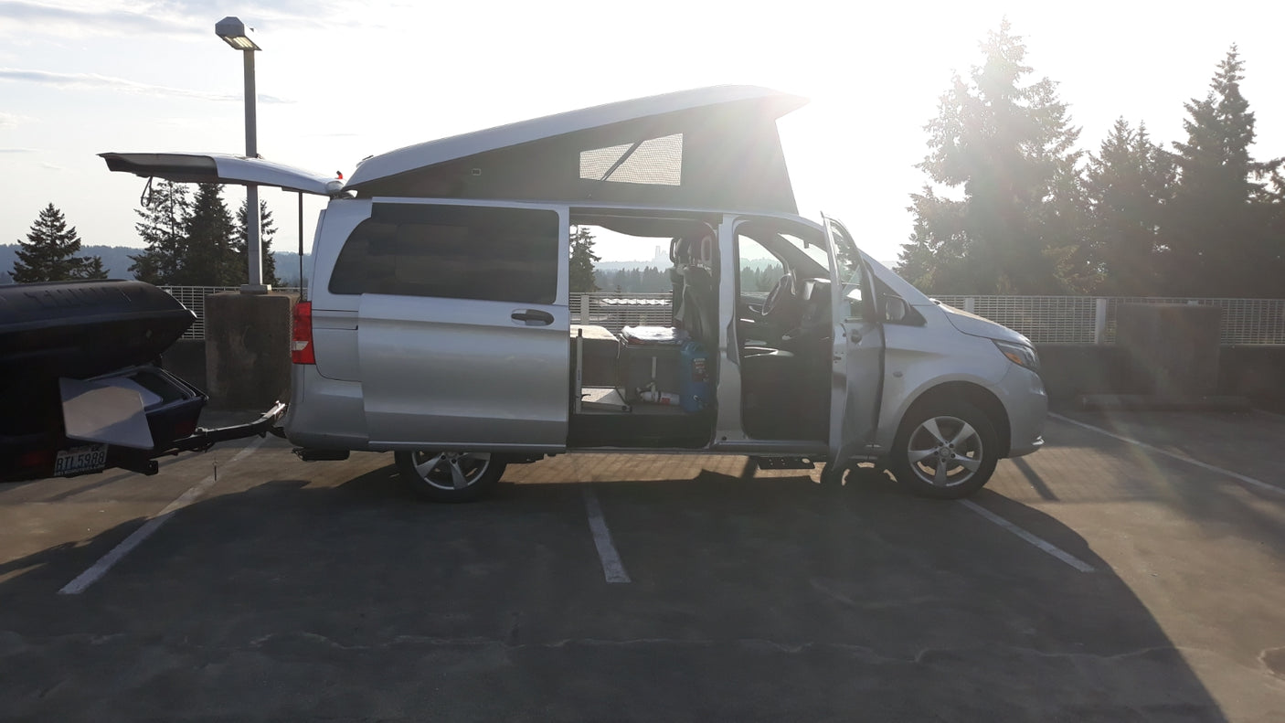 Silver Mercedes Metris pop-top camper van RV rental, open and ready for adventure with its rear trailer.