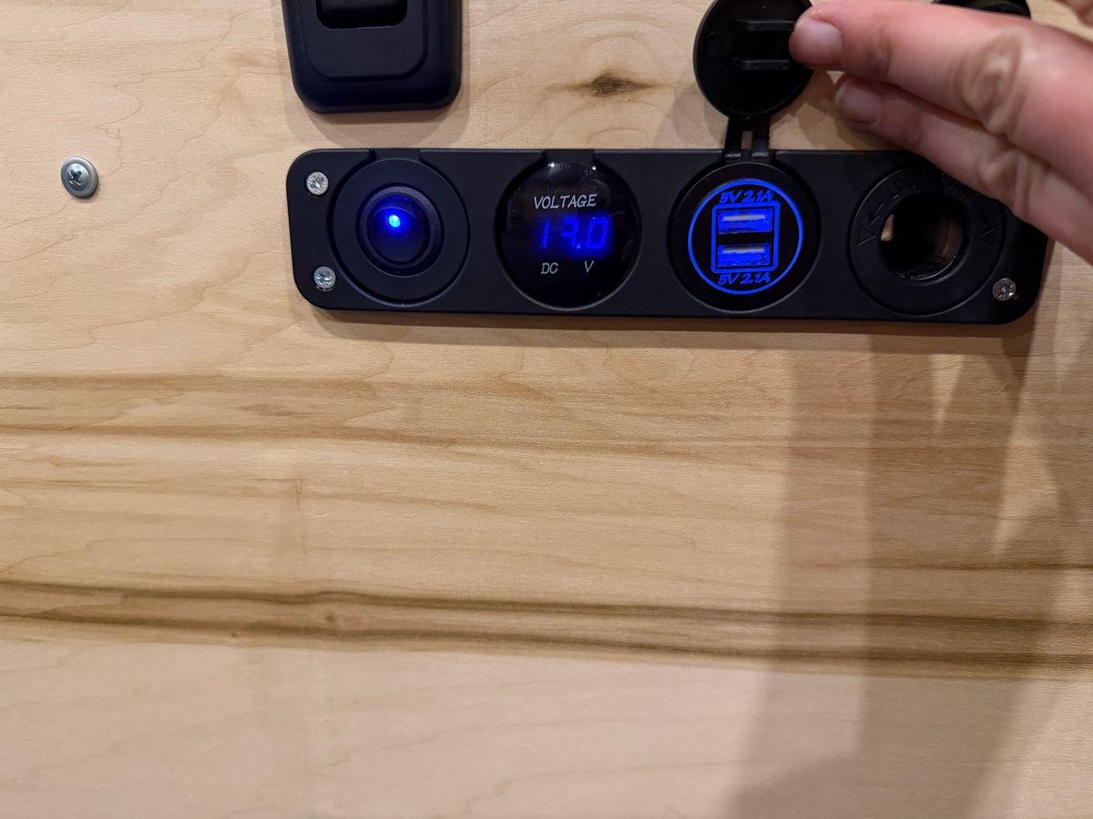 RV rental power panel with 14.0V voltmeter, dual 5V 2.1A USB chargers, and a blue illuminated switch on wood. — photo 7
