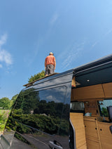 Man on an RV rental roof, admiring the view from his customized camper van. Ideal for adventure travel.