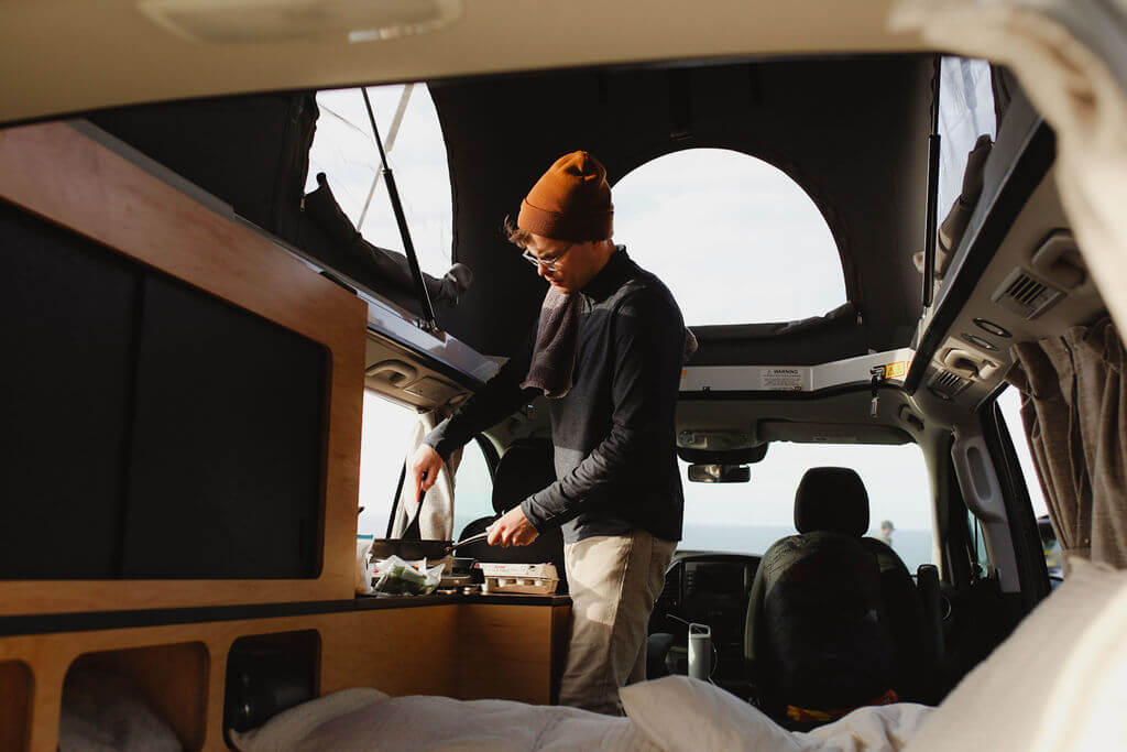  and sea stack.|An RV rental pop-top camper van sits at a misty forest campsite beside a picnic table and a small dog.|This dark blue pop-top campervan — photo 4