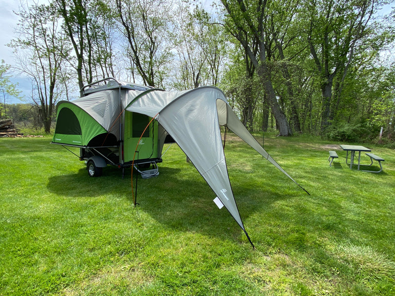 A SylvanSport GO pop-up camper with awning set up on grass. This unique trailer makes an excellent RV rental for camping. — photo 10