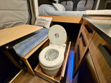 This compact rv rental interior shows a pull-out toilet, a bed, a wooden table, and storage cabinets.