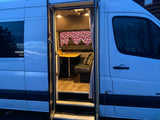 Open side door of an RV rental camper van reveals its cozy, well-lit interior with table and seating, ready for adventures.