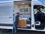 Man photographs the detailed, custom white camper van interior with wood ceiling, cabinets & sink. Perfect for an rv rental.