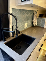 Modern RV rental kitchen featuring a black industrial faucet, sink, and geometric tiled backsplash.