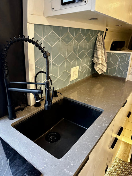 Modern RV rental kitchen featuring a black industrial faucet, sink, and geometric tiled backsplash.
