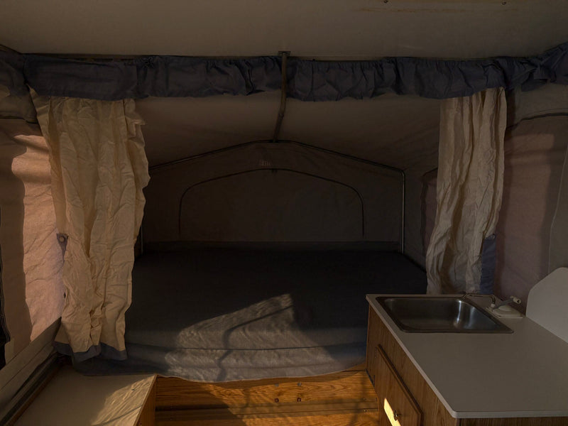 Pop-up RV rental interior with bed, sink, kitchenette, fabric walls & curtains. Light casts shadows. — photo 9