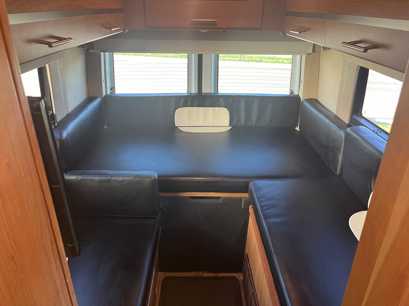 RV rental: Compact interior features convertible black leather seating, overhead cabinets, and rear windows for travel. — photo 10