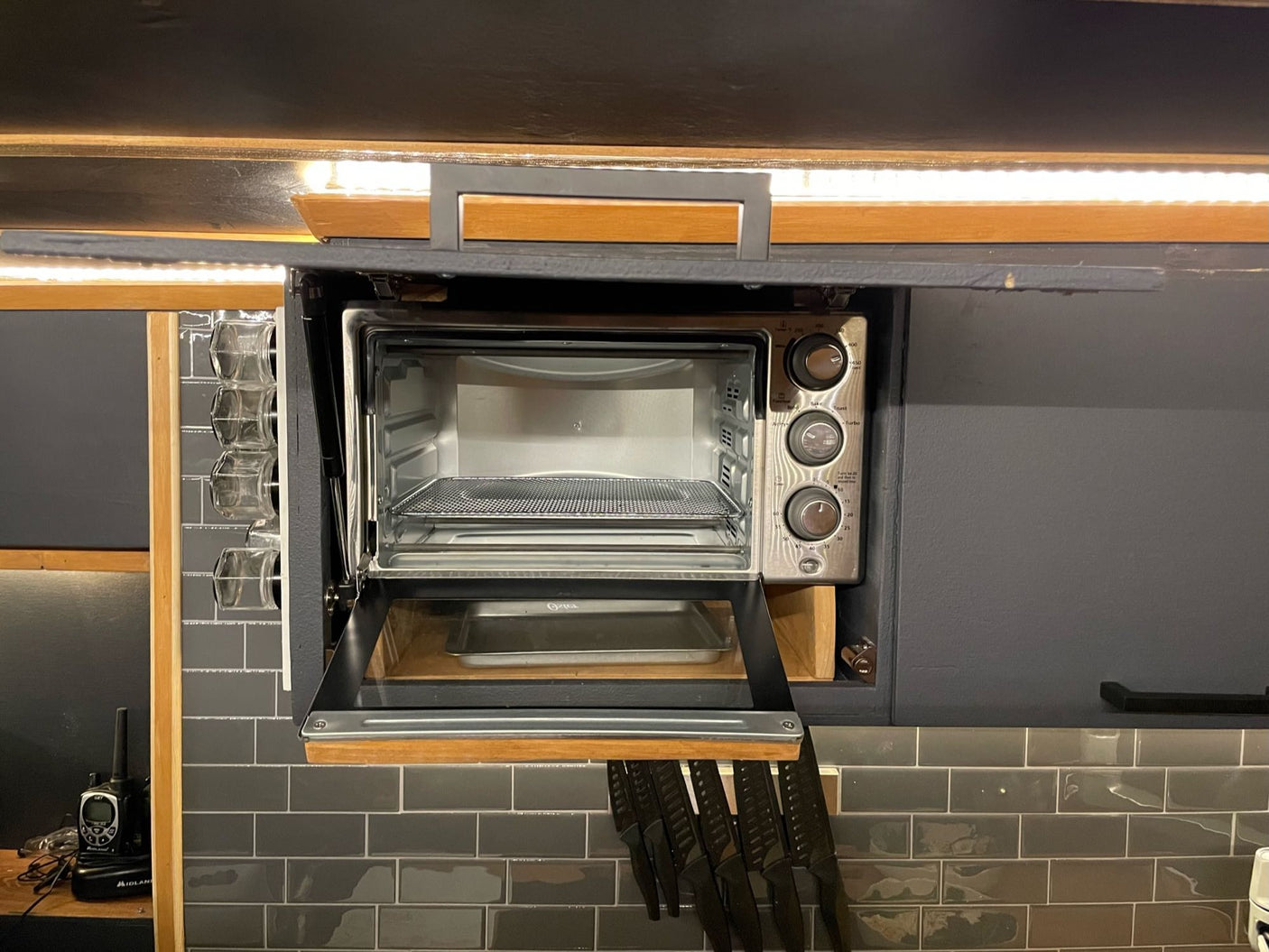 Compact toaster oven built into an RV rental kitchen, ideal for cooking. Features under-cabinet lighting and knife storage.
