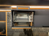 Compact toaster oven built into an RV rental kitchen, ideal for cooking. Features under-cabinet lighting and knife storage.