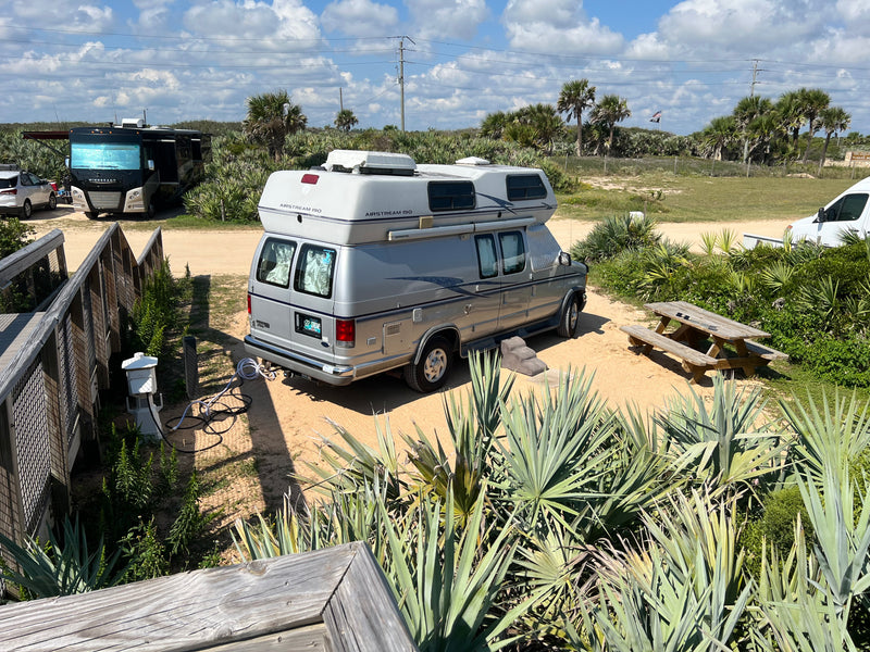 RV rental: Airstream 190 camper van at a sandy Florida campsite by the beach, surrounded by palm trees and a picnic table. — photo 8