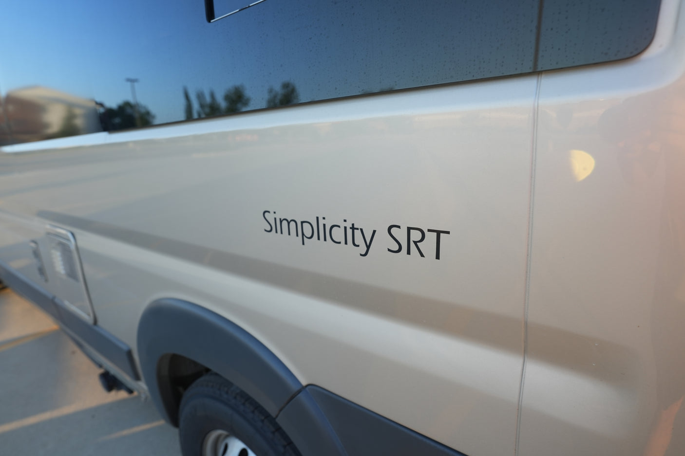 Experience an rv rental! This close-up shows a Simplicity SRT camper van's side in a light color with window reflections.