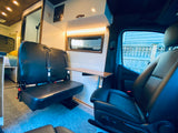 Inside a modern RV rental: front and rear black seats with a versatile table. Perfect camper van setup for travel comfort.