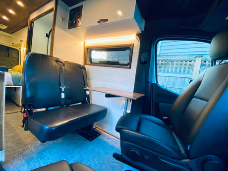 Inside a modern RV rental: front and rear black seats with a versatile table. Perfect camper van setup for travel comfort.