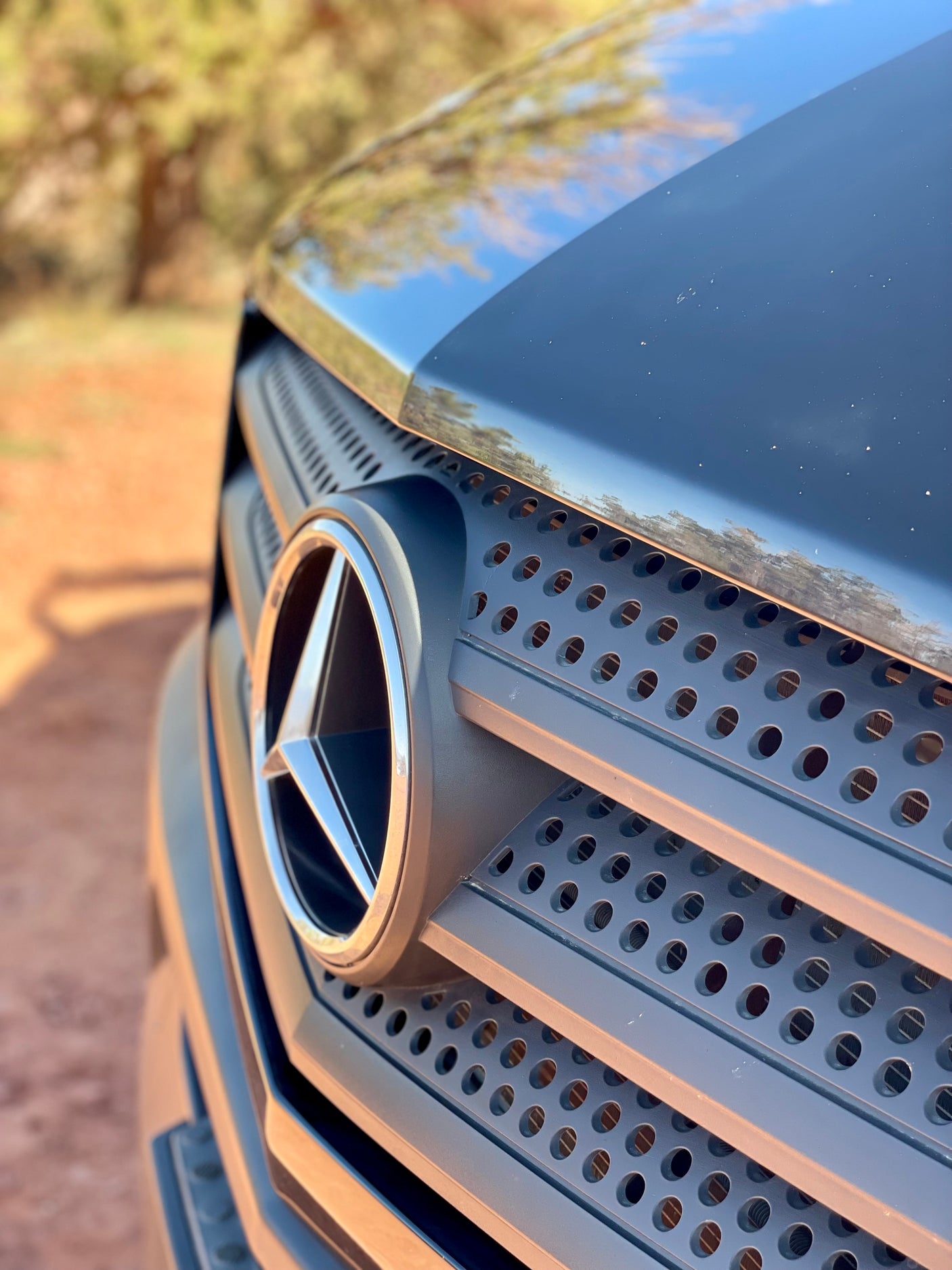 Up-close view of a Mercedes-Benz grille and emblem on an RV rental, set against a blurry outdoor backdrop. Perfect for road trips.