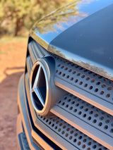 Up-close view of a Mercedes-Benz grille and emblem on an RV rental, set against a blurry outdoor backdrop. Perfect for road trips.