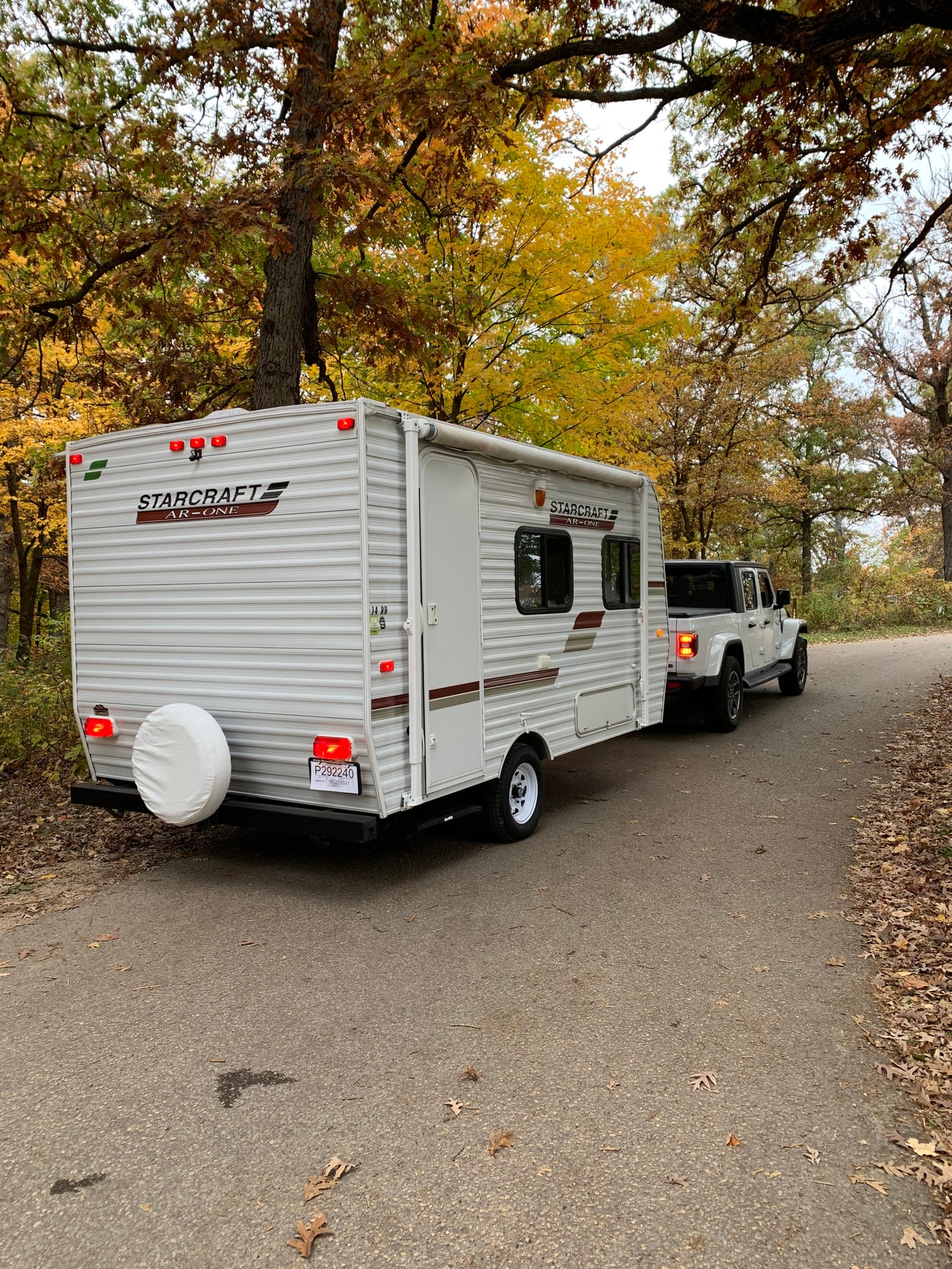 A white Starcraft travel trailer, great for rv rental, is towed by a white Jeep Gladiator on a scenic autumn road.