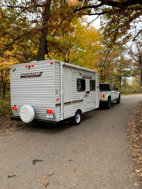 A white Starcraft travel trailer, great for rv rental, is towed by a white Jeep Gladiator on a scenic autumn road.