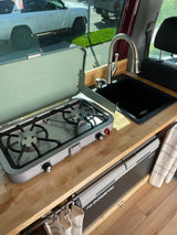 RV rental interior: A compact kitchen setup with a Coleman stove, black sink, and Dometic CFX cooler.