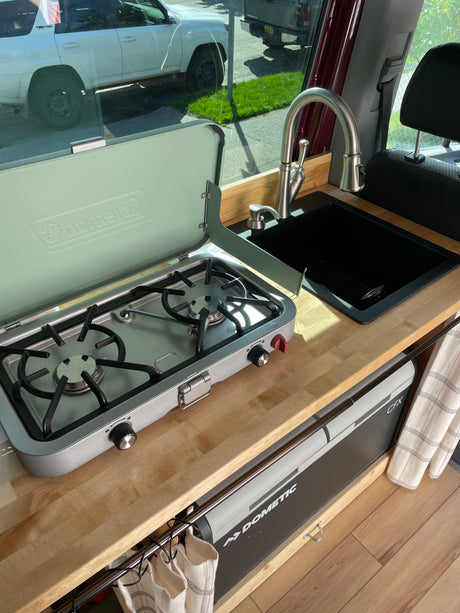 RV rental interior: A compact kitchen setup with a Coleman stove, black sink, and Dometic CFX cooler.