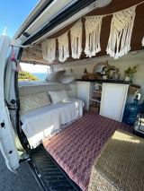 Cozy RV rental interior with boho decor, featuring a bed, seating, and an ocean view from the open back.