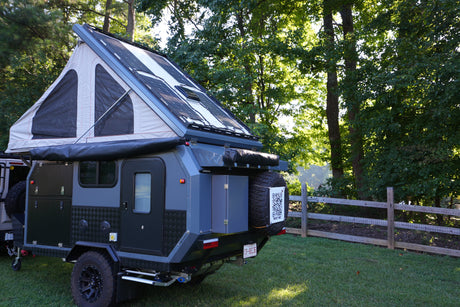 Rugged overland trailer with pop-up tent and solar panels, available for RV rental, parked in a scenic outdoor setting.