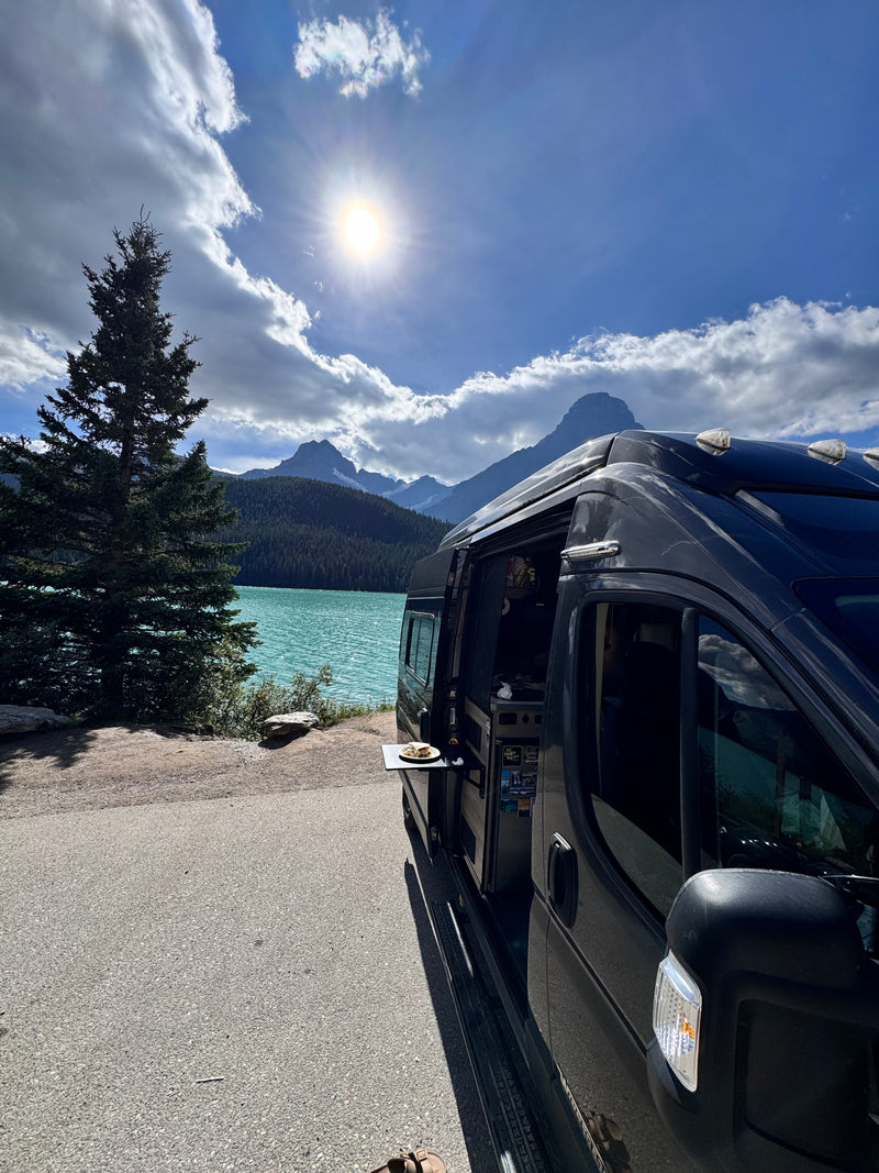 RV rental parked by a vivid turquoise lake, towering mountains. Enjoying a meal on the van's pull-out table under sunny skies. — photo 18