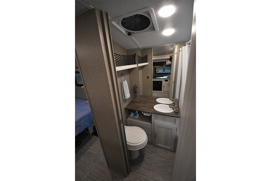 RV rental: Compact interior shows a bathroom with dual sinks, toilet, and overhead fan. A blue bed is visible left. — photo 4