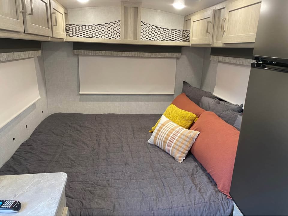 Inviting RV rental bedroom: bed with grey comforter & colorful pillows, overhead cabinets, and window blinds. — photo 9